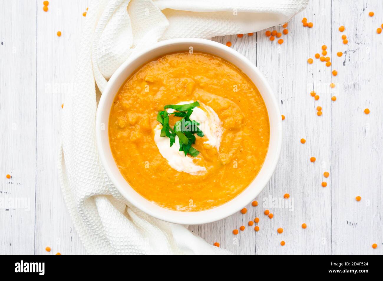 Ciotola di zuppa di lenticchie vegetariane con carote, succo d'arancia, crema fraiche e prezzemolo Foto Stock