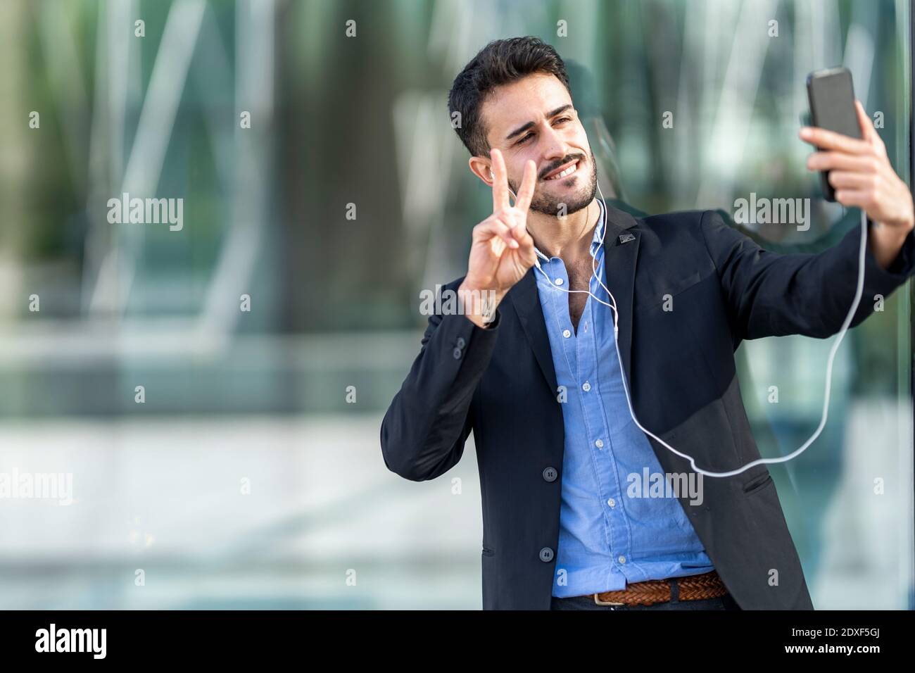 Uomo d'affari sicuro che mostra il segno di pace mentre prende selfie Foto Stock