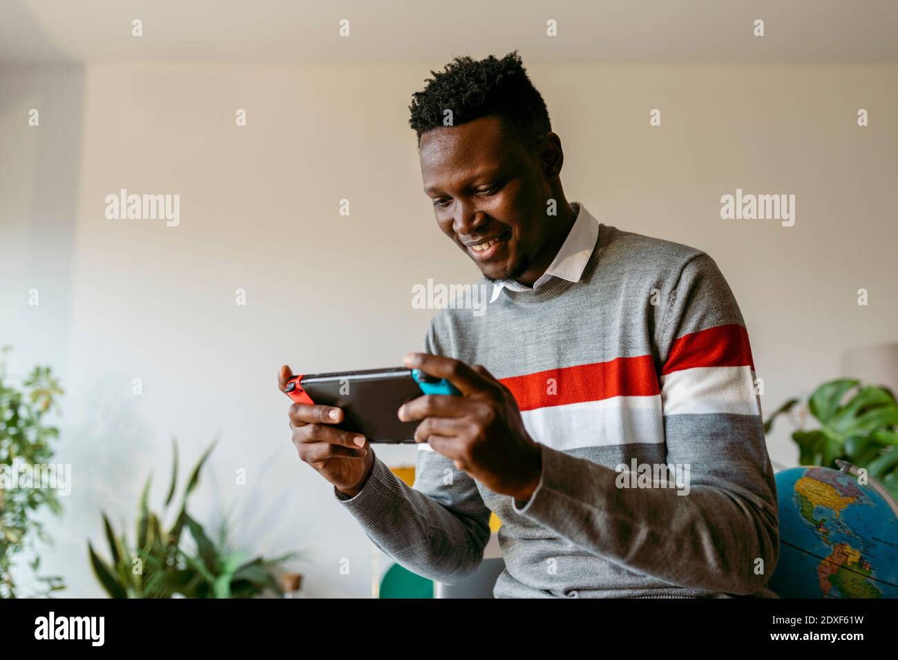 Uomo d'affari sorridente che gioca a un videogioco portatile a casa durante pausa dal lavoro Foto Stock