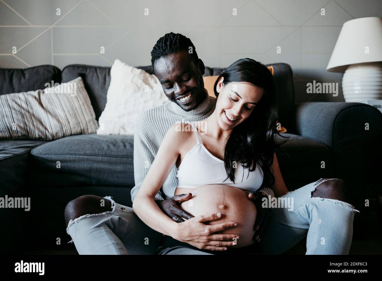 Giovane uomo con donna incinta che guarda l'addome a casa Foto Stock