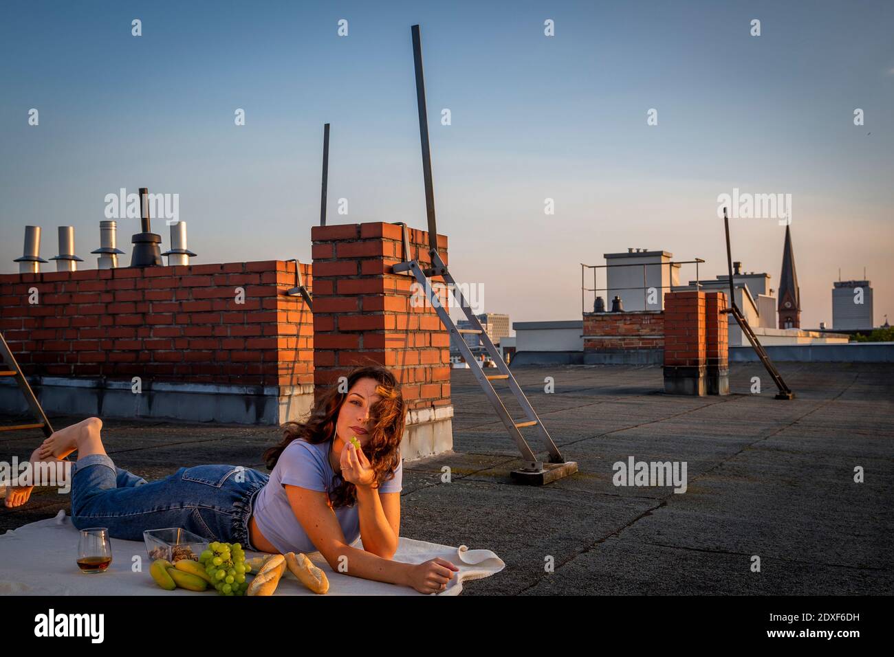 Donna delle brunette che mangia frutta, facendo un picnic sul tetto al tramonto Foto Stock