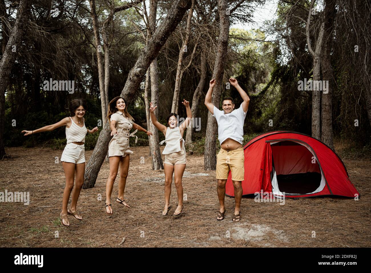 Famiglia allegra che salta nella foresta contro al campeggio durante la vacanza Foto Stock