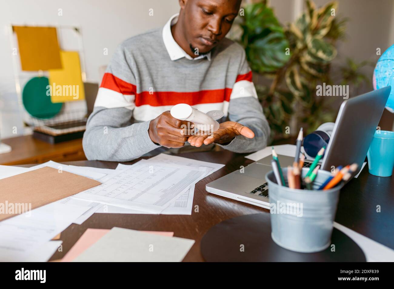 Freelance maschile che applica l'igienizzatore per le mani durante il lavoro da casa Foto Stock