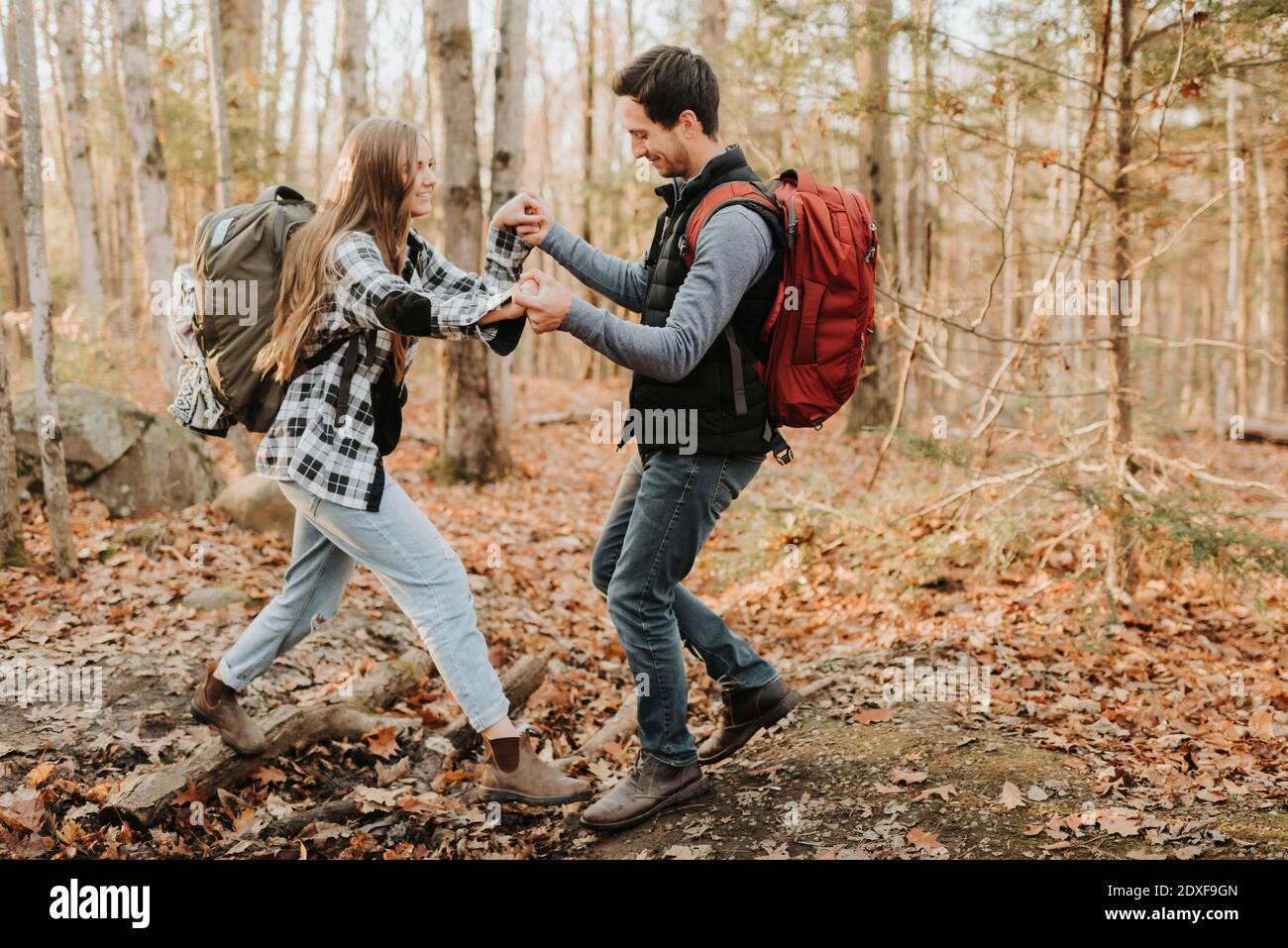 Giovane uomo che aiuta la ragazza durante l'escursione nella foresta d'autunno Foto Stock