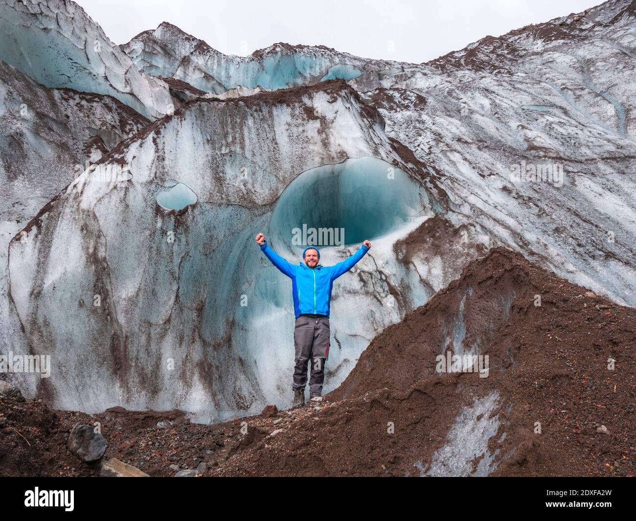 Felice uomo medio adulto in piedi sulla cresta di montagna con le braccia sollevate contro il ghiacciaio a Svinafellsjokull, Islanda Foto Stock