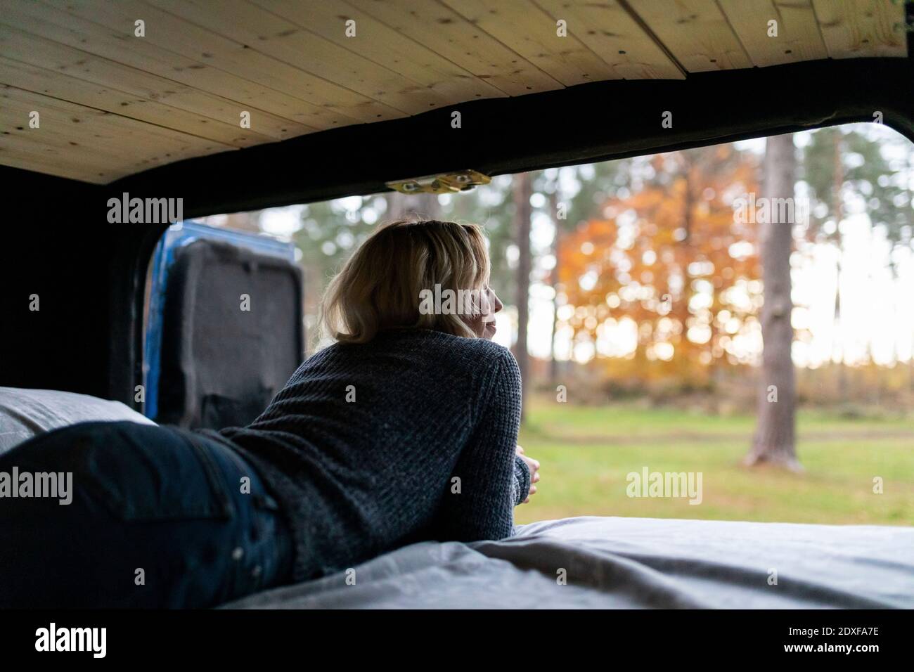Donna confortevole che guarda all'esterno mentre si sdraiava sul letto in camper furgone Foto Stock