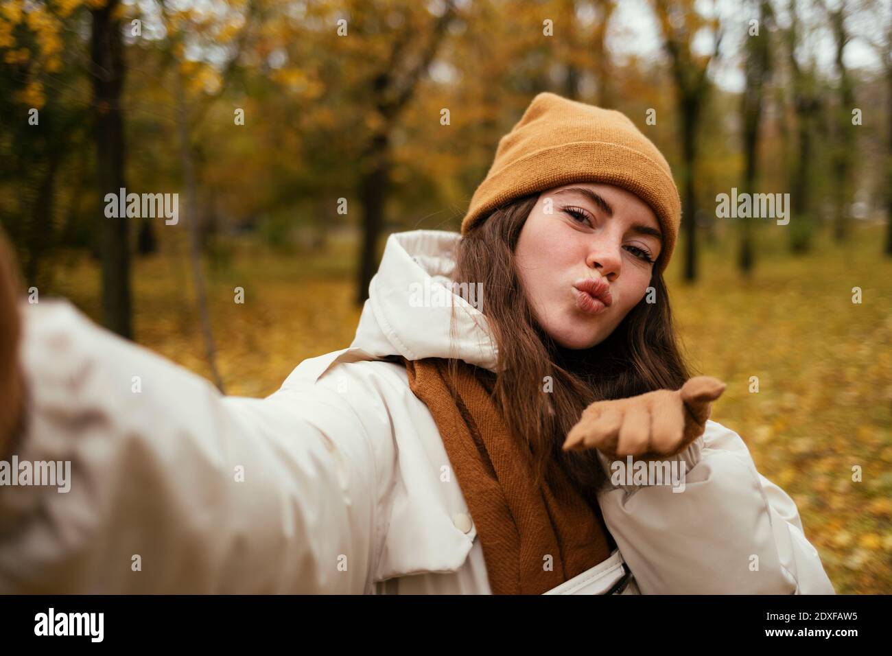 Bella giovane donna che soffia bacio mentre prendendo selfie in autunno parcheggio Foto Stock