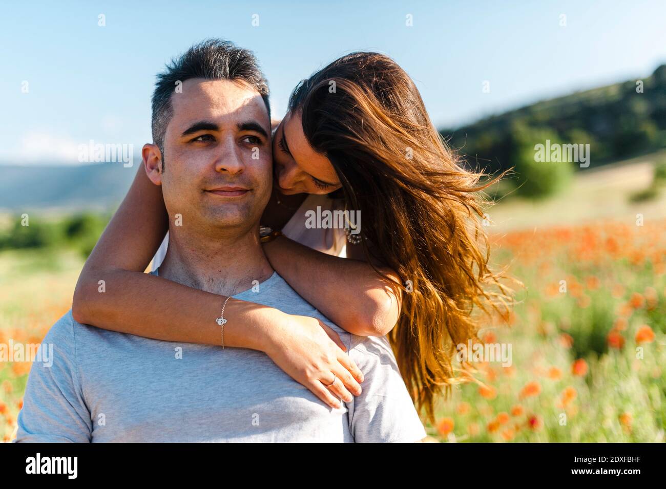 Fidanzata abbracciando il ragazzo da dietro a campo agricolo durante la primavera Foto Stock