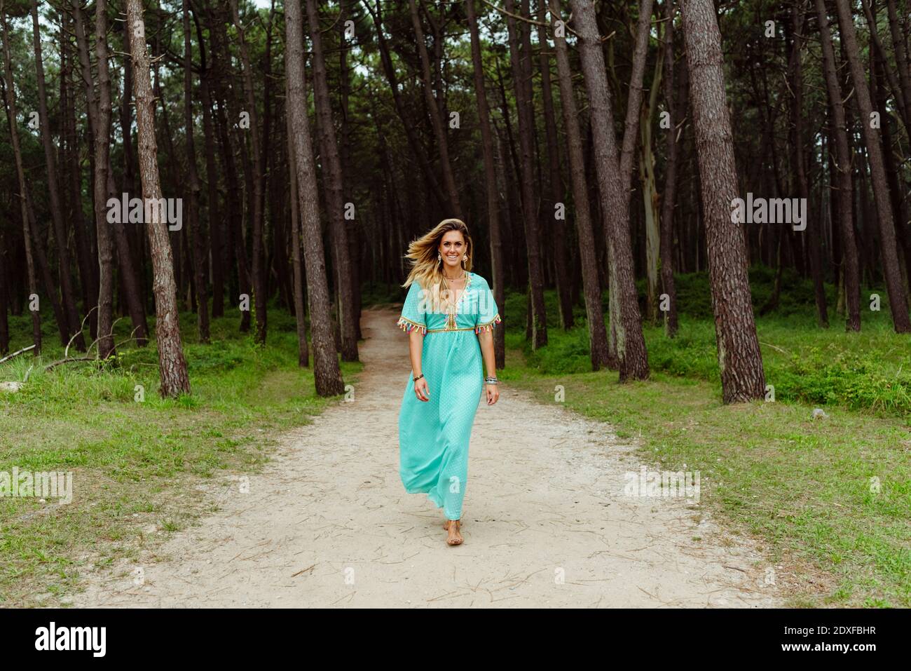 Donna mid adulta sorridente mentre cammina lungo il sentiero della foresta Foto Stock