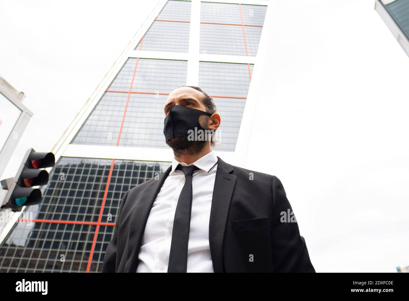 Uomo d'affari che indossa una maschera protettiva contro il moderno grattacielo Foto Stock