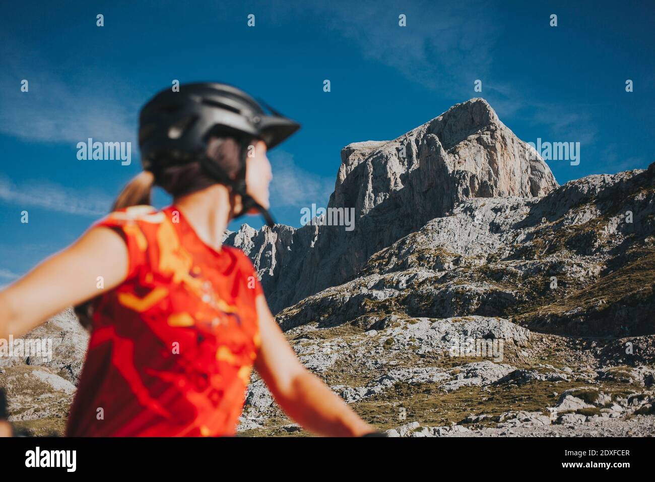 Ciclista femminile che guarda la montagna rocciosa in giornata di sole, Parco Nazionale Picos de Europa, Cantabria, Spagna Foto Stock