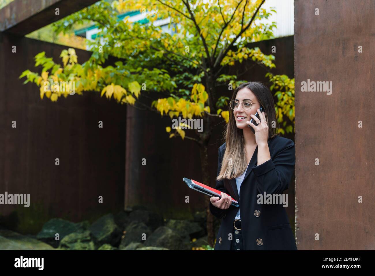 Sorridente imprenditore femminile che parla al telefono mentre si è in piedi di marrone parete Foto Stock