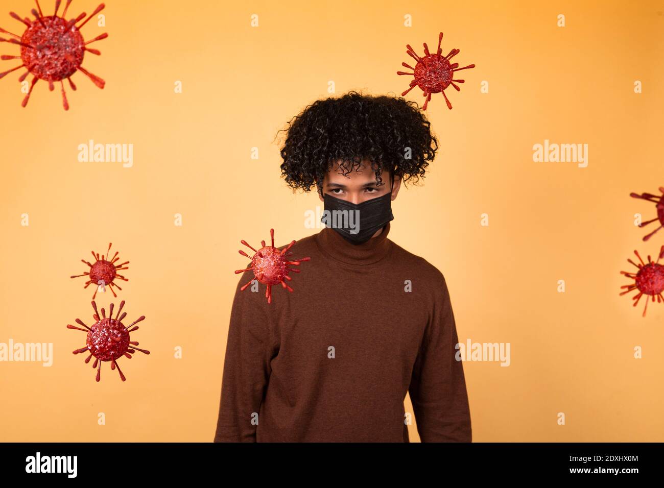 Afro giovane uomo con una maschera medica su sfondo giallo guardando alcune molecole di batteri. Epidemia, virus, salute. Spazio di copia Foto Stock