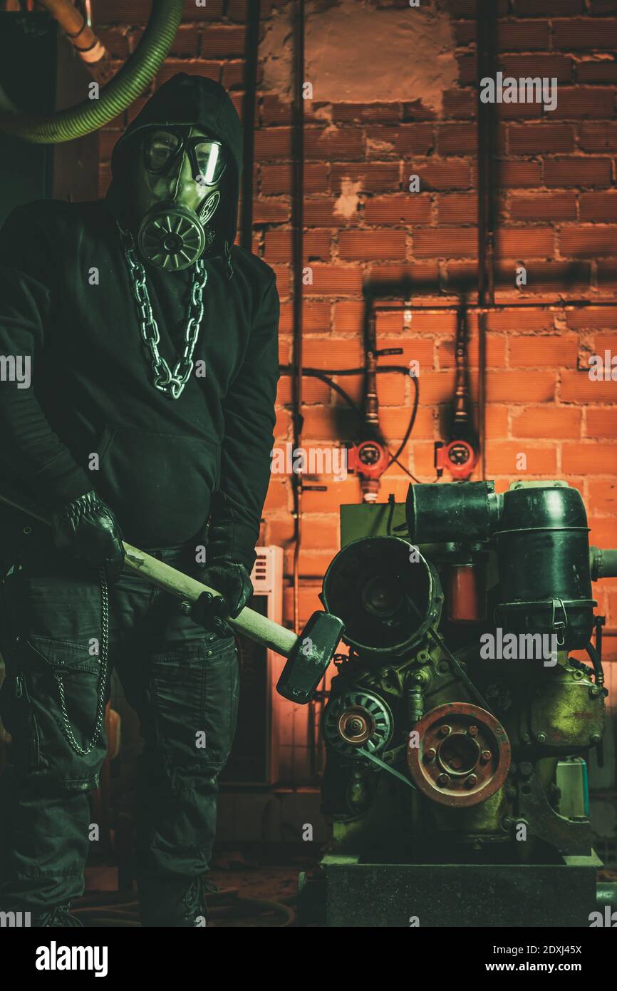 Uomo con maschera a gas e martello in sala macchine. Concetto di pericolo nucleare, biologico e chimico. Foto Stock
