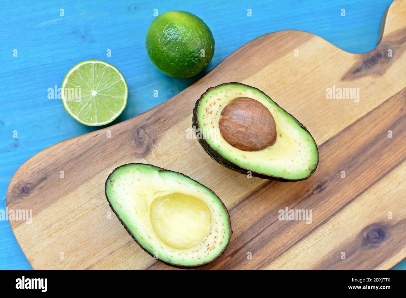 Piatto superiore con avocado tagliato, lime su piatto di legno e fondo blu. Foto Stock