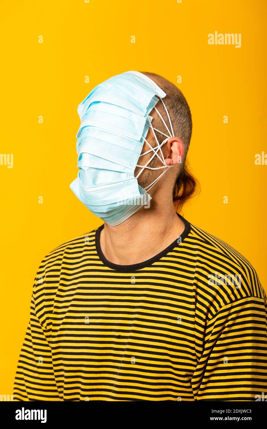 Uomo adulto che indossa maschere chirurgiche che coprono tutto il suo viso su sfondo giallo Foto Stock