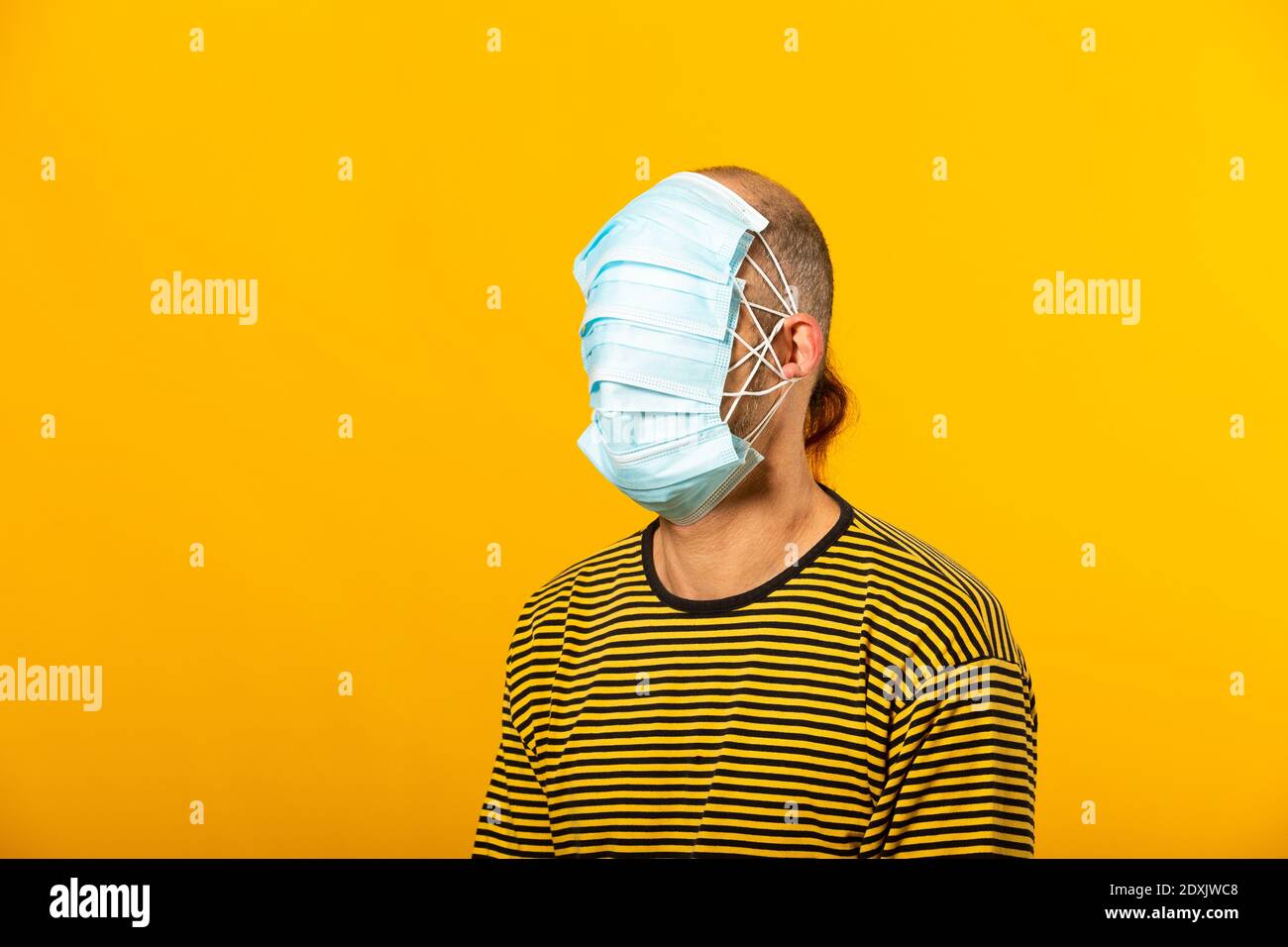 Uomo adulto che indossa maschere chirurgiche che coprono tutto il suo viso su sfondo giallo Foto Stock Uomo adulto che indossa maschere chirurgiche che coprono tutto il suo viso su sfondo giallo Foto Stock