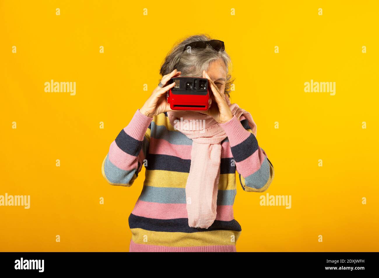 Donna anziana in abiti casual scattando una foto con un fotocamera istantanea su sfondo giallo Foto Stock