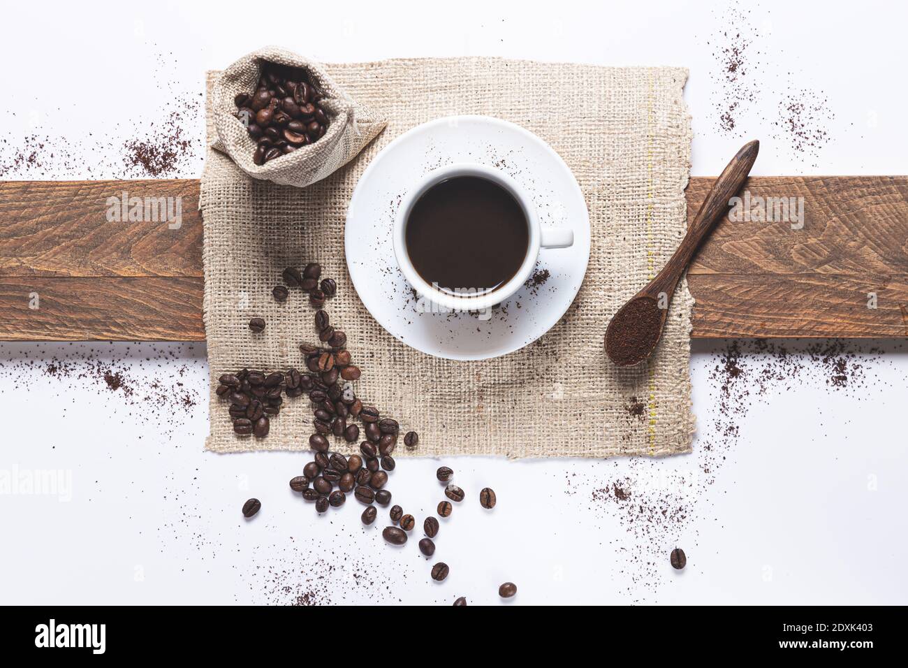 tazza di caffè bianca, chicchi di caffè fuoriuscito dalla borsa, cucchiaio di legno con caffè su fondo bianco. Vista dall'alto. Foto Stock