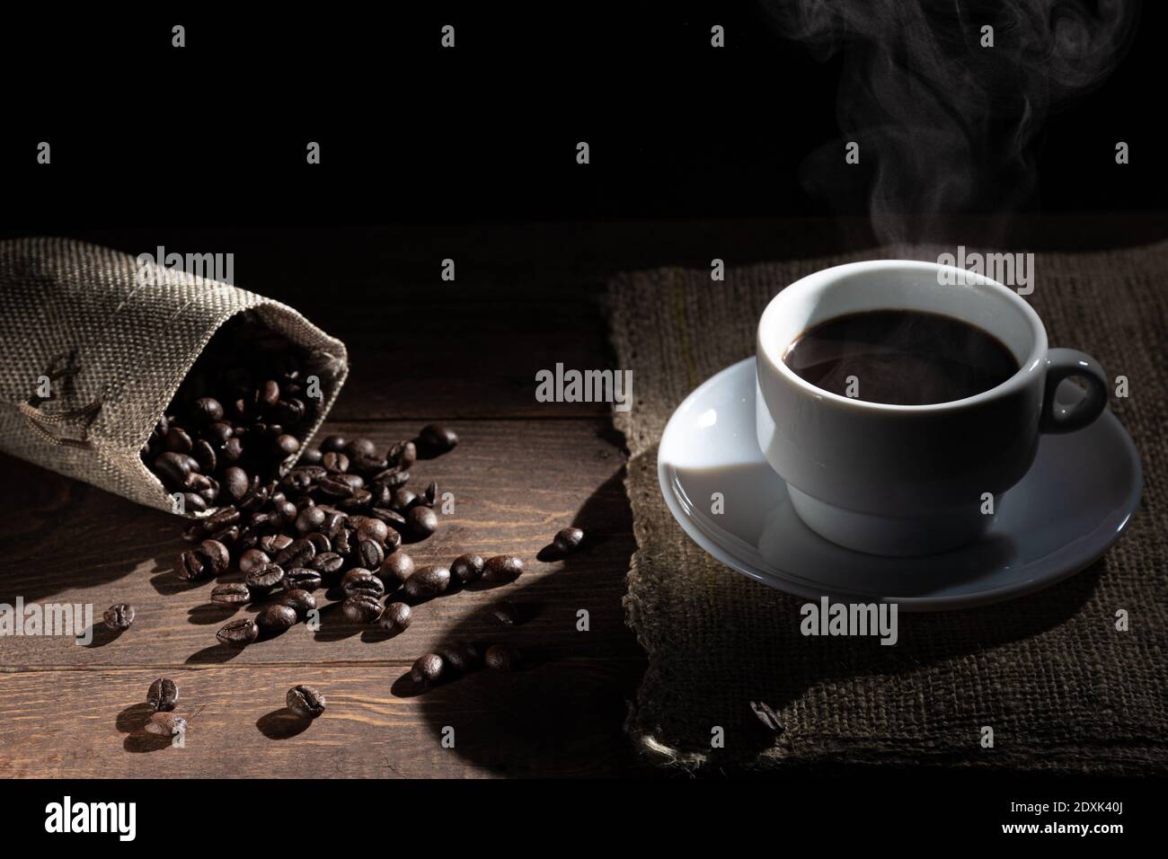 Tazza bianca di caffè, chicchi di caffè fuoriuscito dalla confezione su un tavolo di legno su sfondo nero. Foto Stock