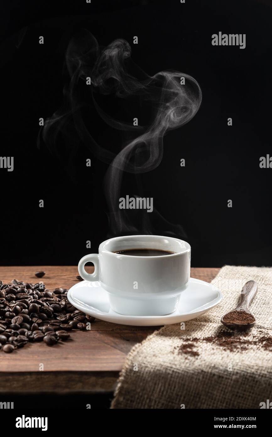 Caffè caldo affumicato, con chicchi di caffè. Cucchiaio di legno con caffè su base di legno, su sfondo scuro. Foto Stock