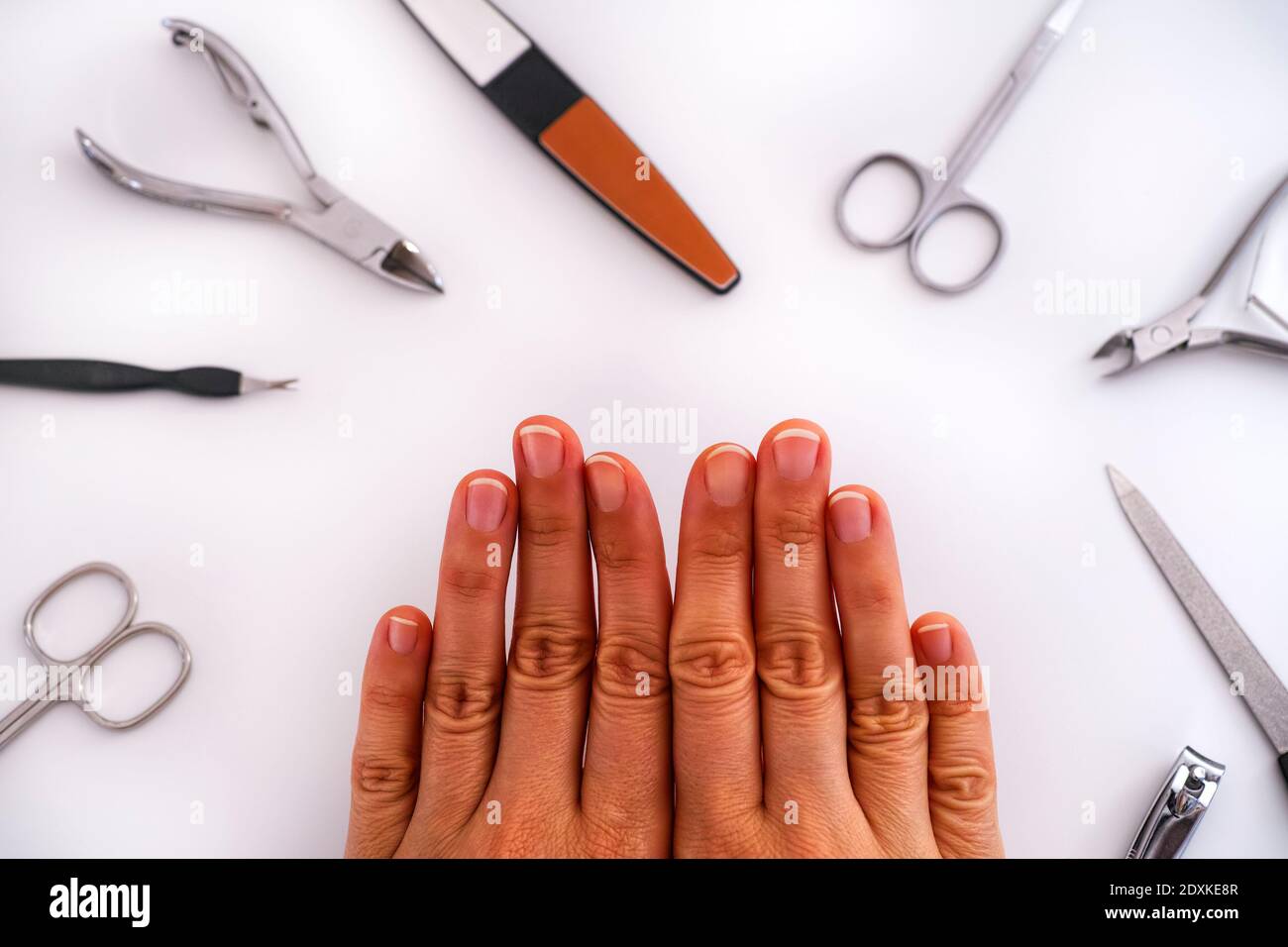 Le mani della donna con manicure non rivestito e gli attrezzi domestici di manicure. Sfondo bianco. Foto Stock