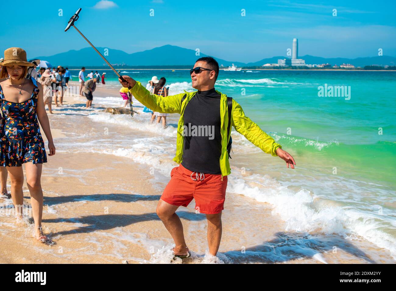 Sanya, Provincia di Hainan, Cina. Felice ragazzo asiatico sorridente prende un selfie sulla spiaggia contro il mare bello. Mare panoramico. Foto Stock