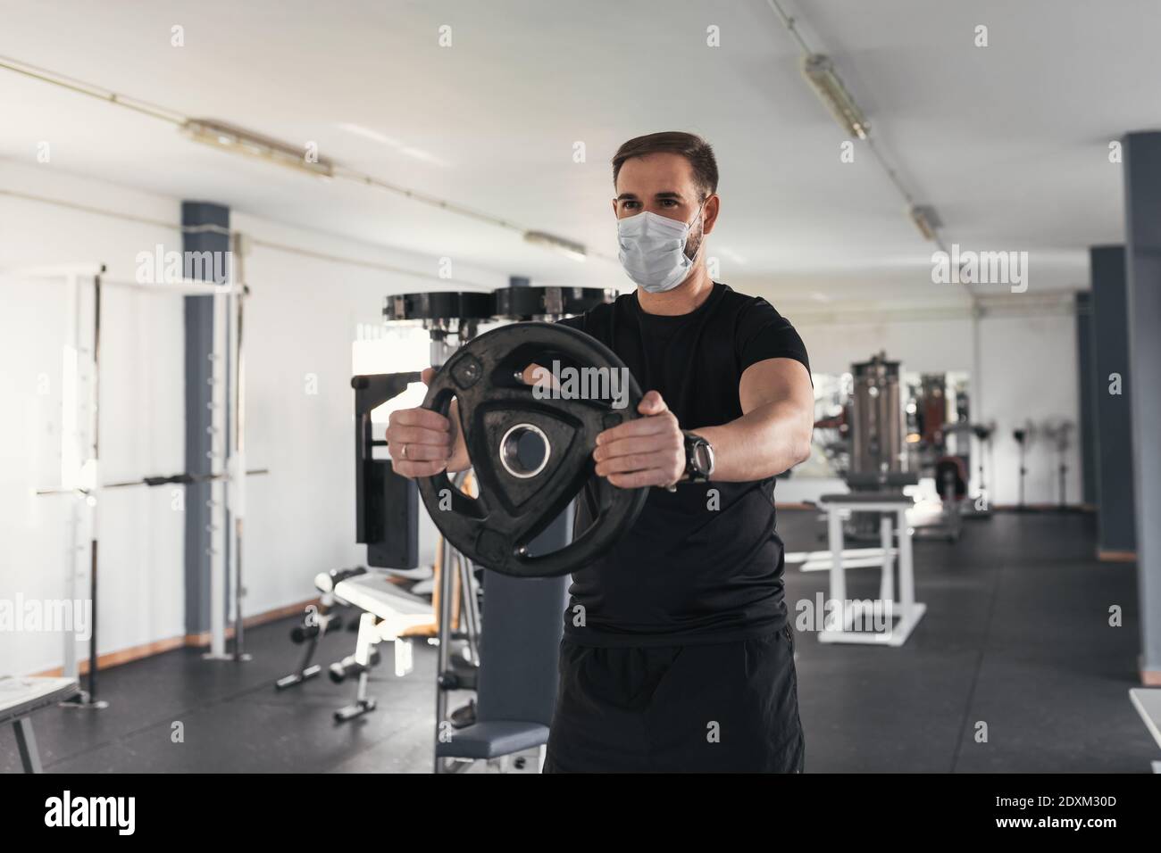 Uomo che si adopera indossando la maschera in palestra, COVID-19 pandemico regole di distanziamento sociale mentre si lavora in palestra interna riaperta. Foto Stock