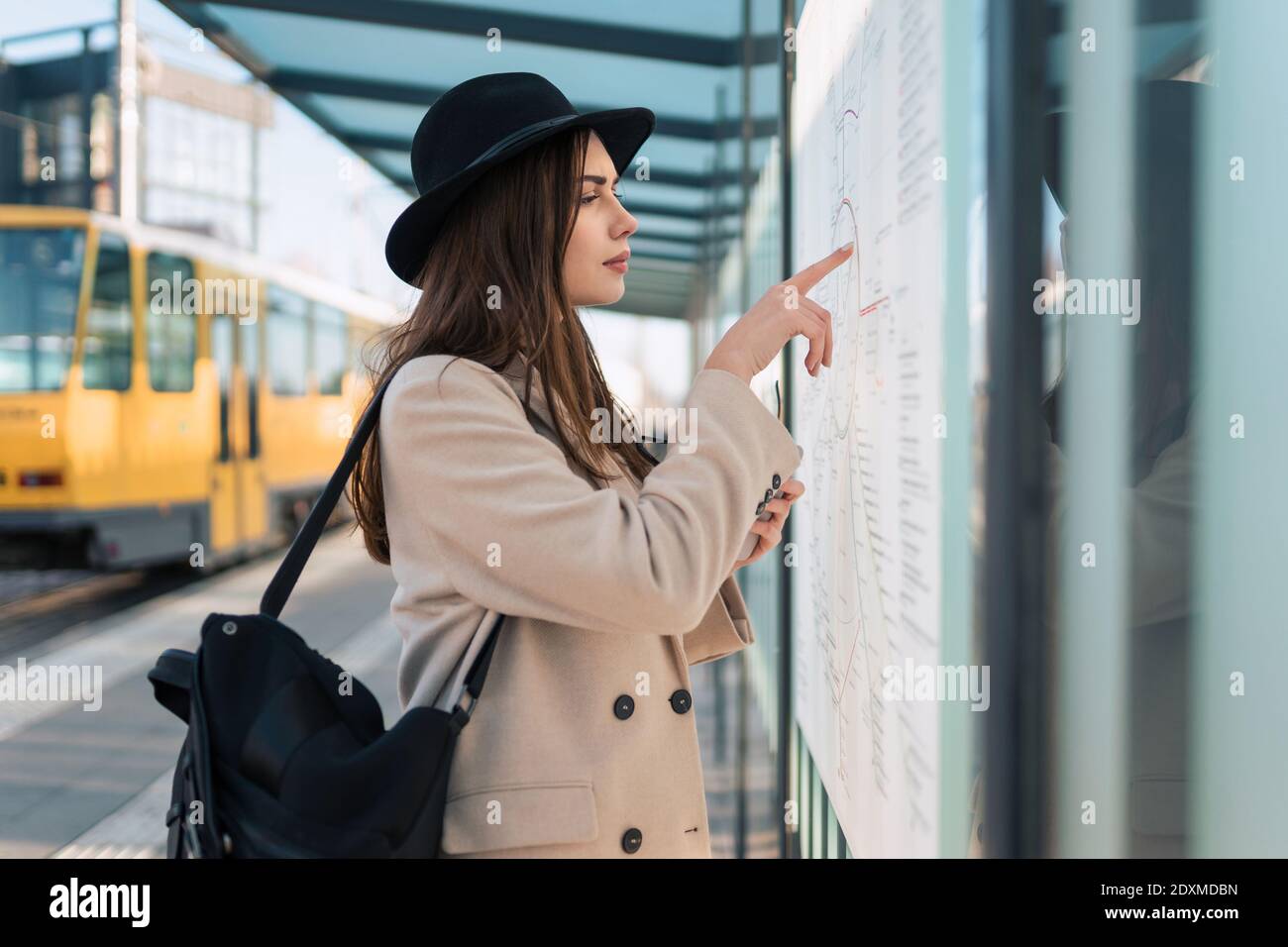 Donna turistica alla fermata dell'autobus guardando sulla mappa del pubblico percorsi di trasporto Foto Stock