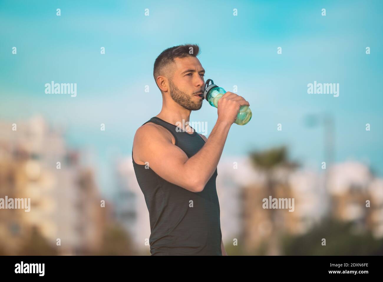 Giovane uomo in forma fisica che beve acqua da una bottiglia riutilizzabile durante un allenamento. Bere mentre si esercita. Disidratazione durante l'esercizio Foto Stock