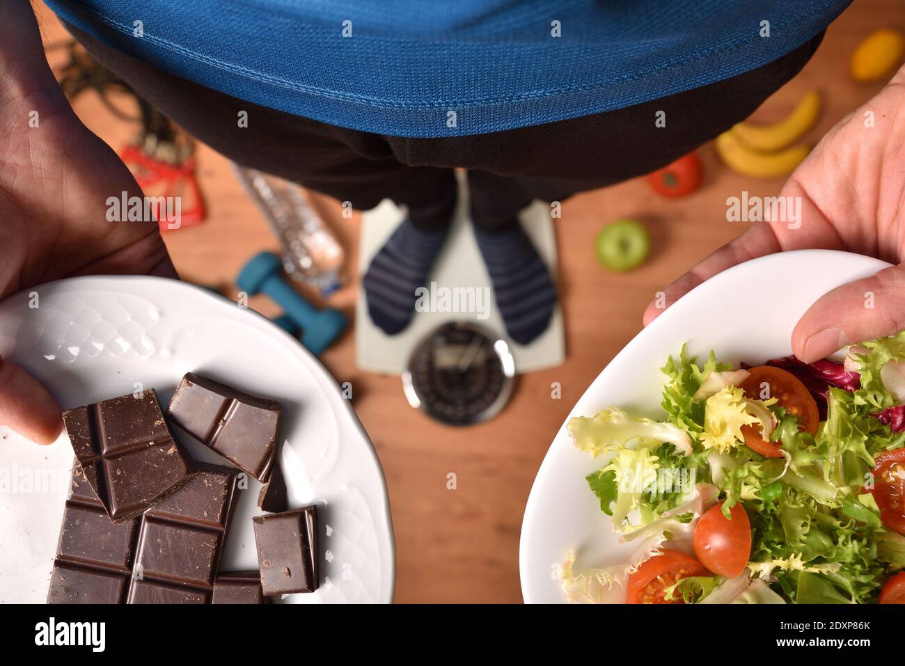 Persona su una scala che mostra il piatto di confronto con insalata come cibo sano e cioccolato come cibo malsano. Vista dall'alto Foto Stock