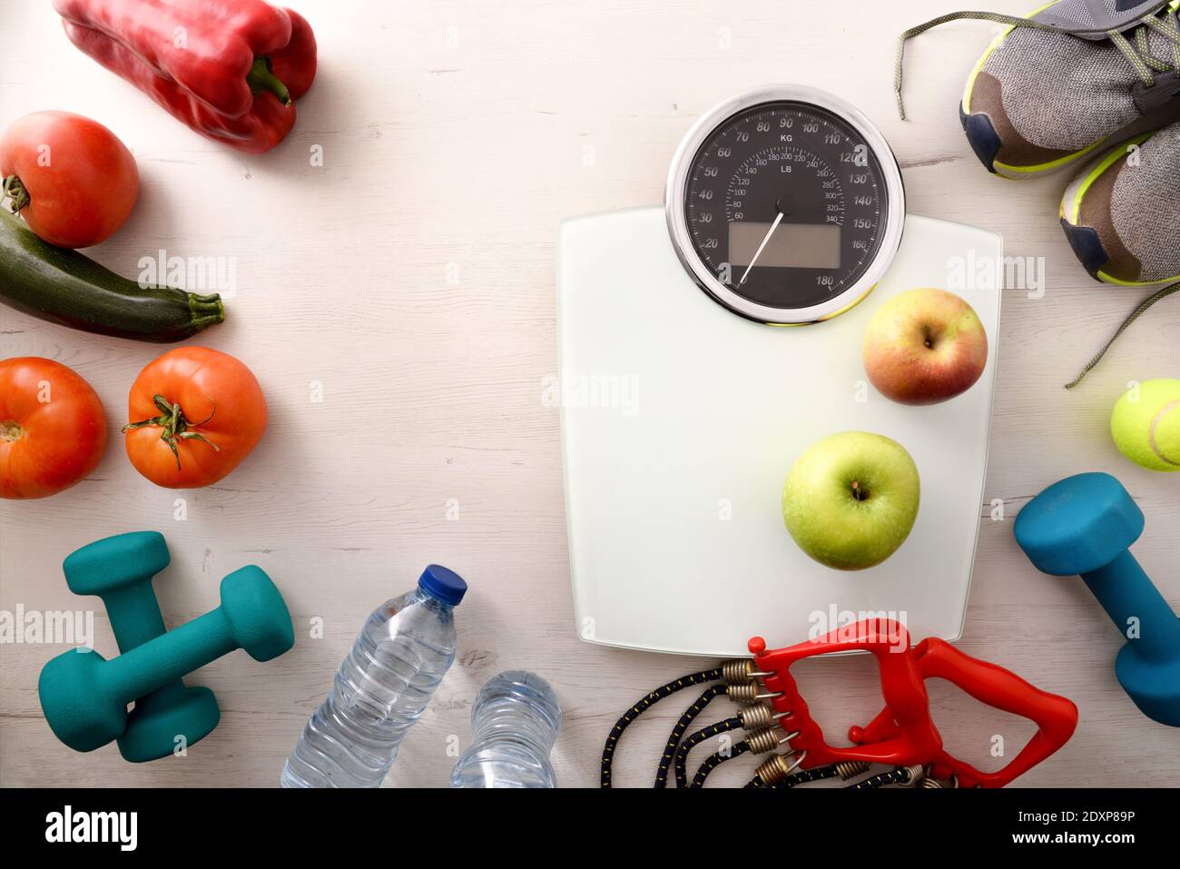 Cibo sano e sportivo per il benessere con accessori, frutta e verdura e bilancia su tavola di legno. Vista dall'alto. Composizione orizzontale. Foto Stock