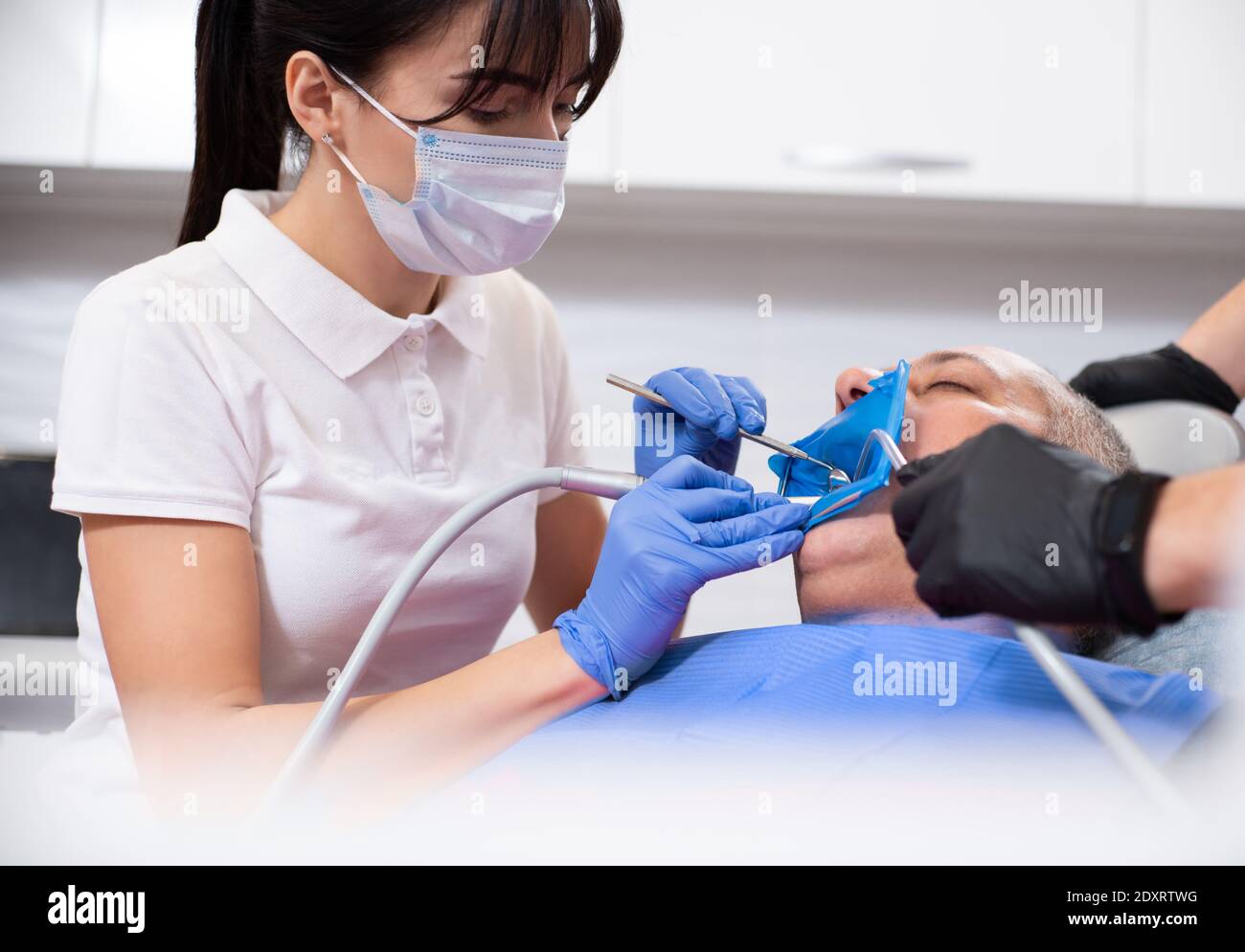 Dentista femminile che indossa una maschera medica ptotettiva che tratta un paziente in uno studio dentistico. Foto Stock