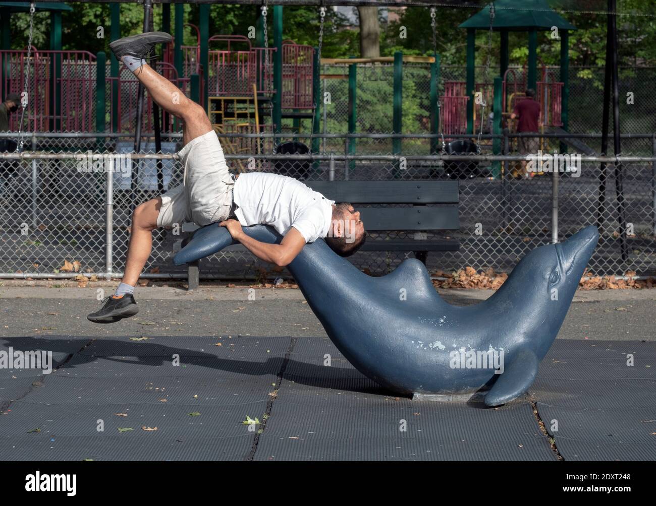 Un immigrato dal Bangladesh fa una routine di esercizi di stretching su una statua di un delfino in Kissena Park a Flushing, New York City. Foto Stock