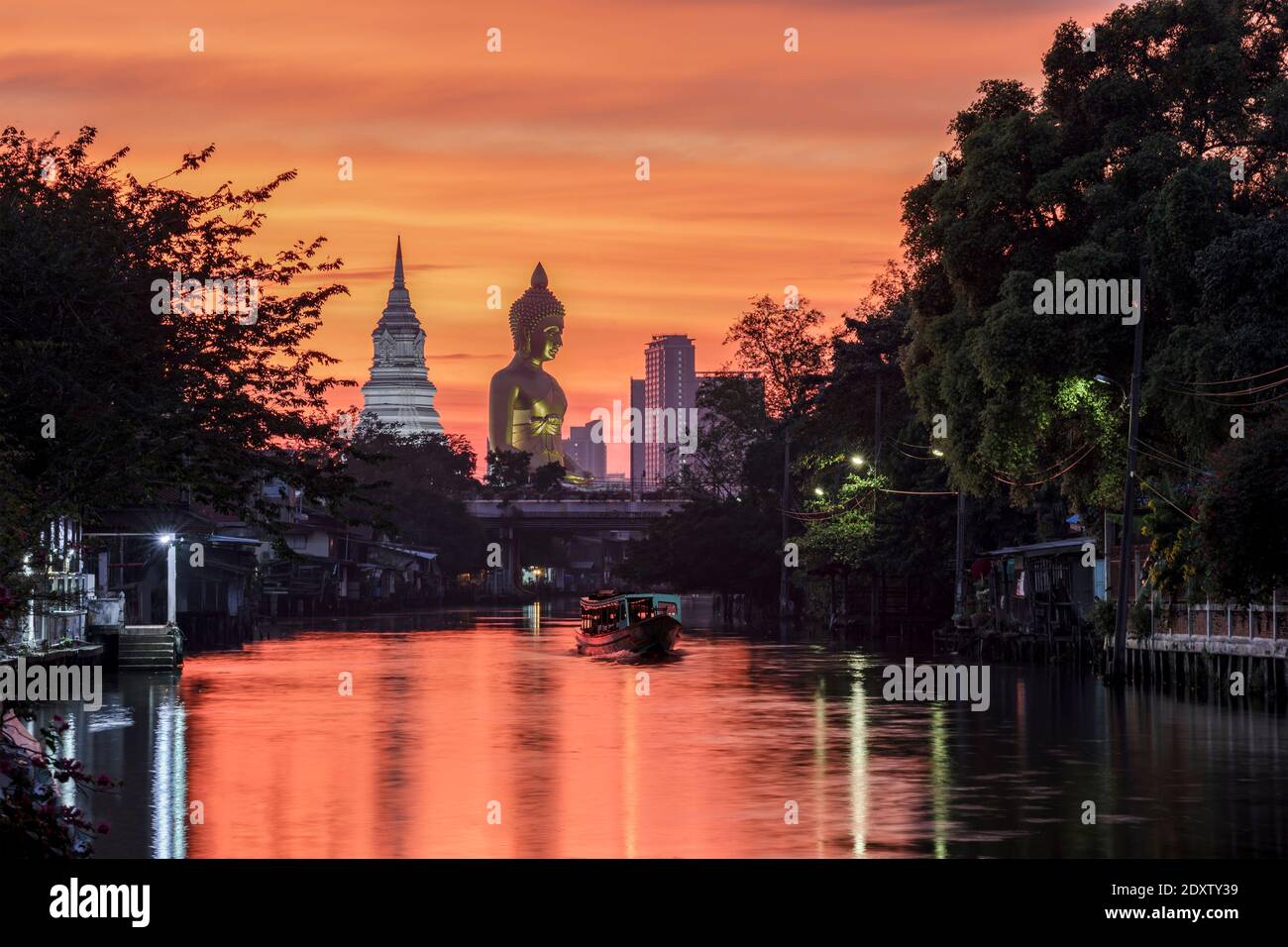 Una barca passava la statua del Grande Buddha (Phra Buddha Dhammakaya Thepmongkhon) nel tempio Wat Pak Nam Phasi Charoen situato vicino al fiume durante il tramonto. Foto Stock
