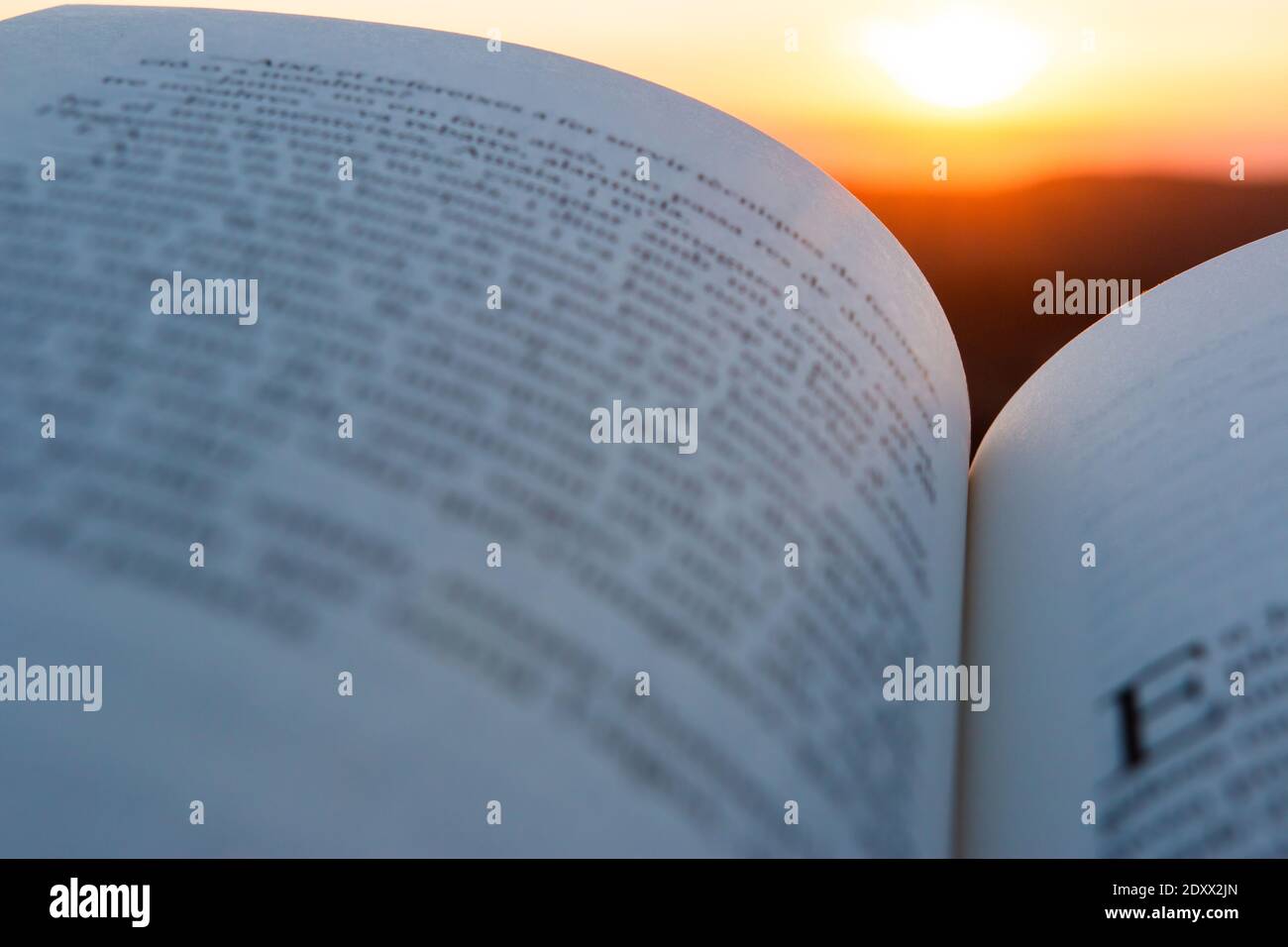 Pagine di un libro aperto con testo illeggibile sfocato con tramonto o sole alba sullo sfondo. Ispirazione, creatività, lettura, idee e imagina Foto Stock