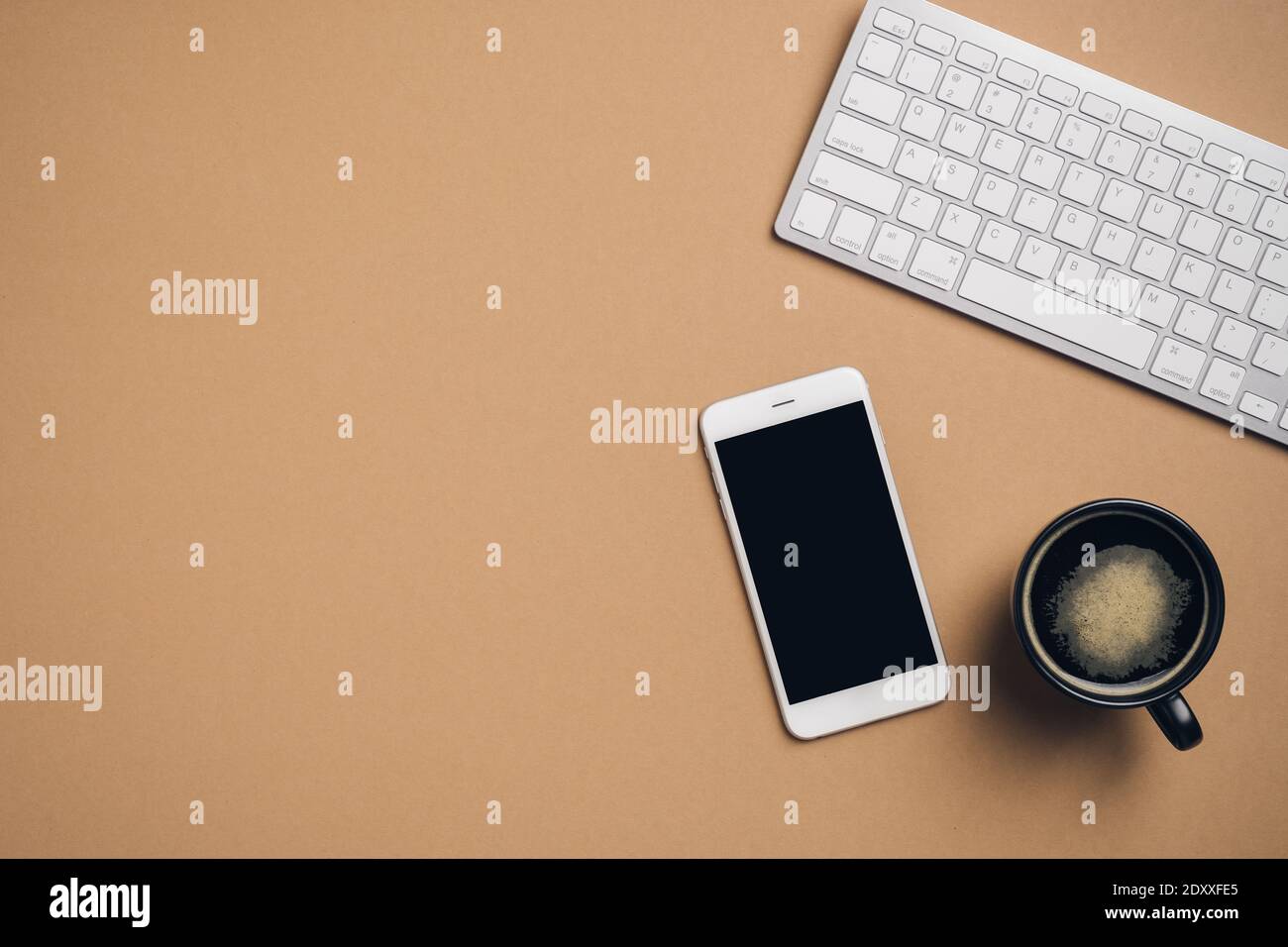 Spazio di lavoro minimalista con tastiera per computer, smartphone con mockup a schermo vuoto, tazza di caffè su sfondo marrone. Vista dall'alto con spazio per la copia. Foto Stock