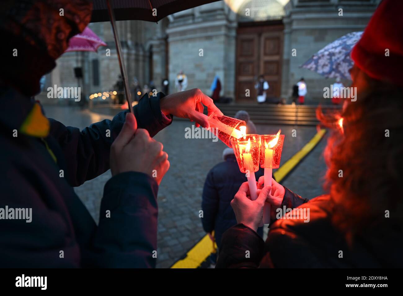 Weingarten, Germania. 24 Dic 2020. Molti bambini fanno la storia di Natale sul piazzale della Basilica, mentre in primo piano un uomo accende la candela su un'altra candela. La candela era accesa con la luce di Bethehem. Circa 200 persone guardano lo spettacolo sotto la pioggia. Credit: Felix Kästle/dpa/Alamy Live News Foto Stock