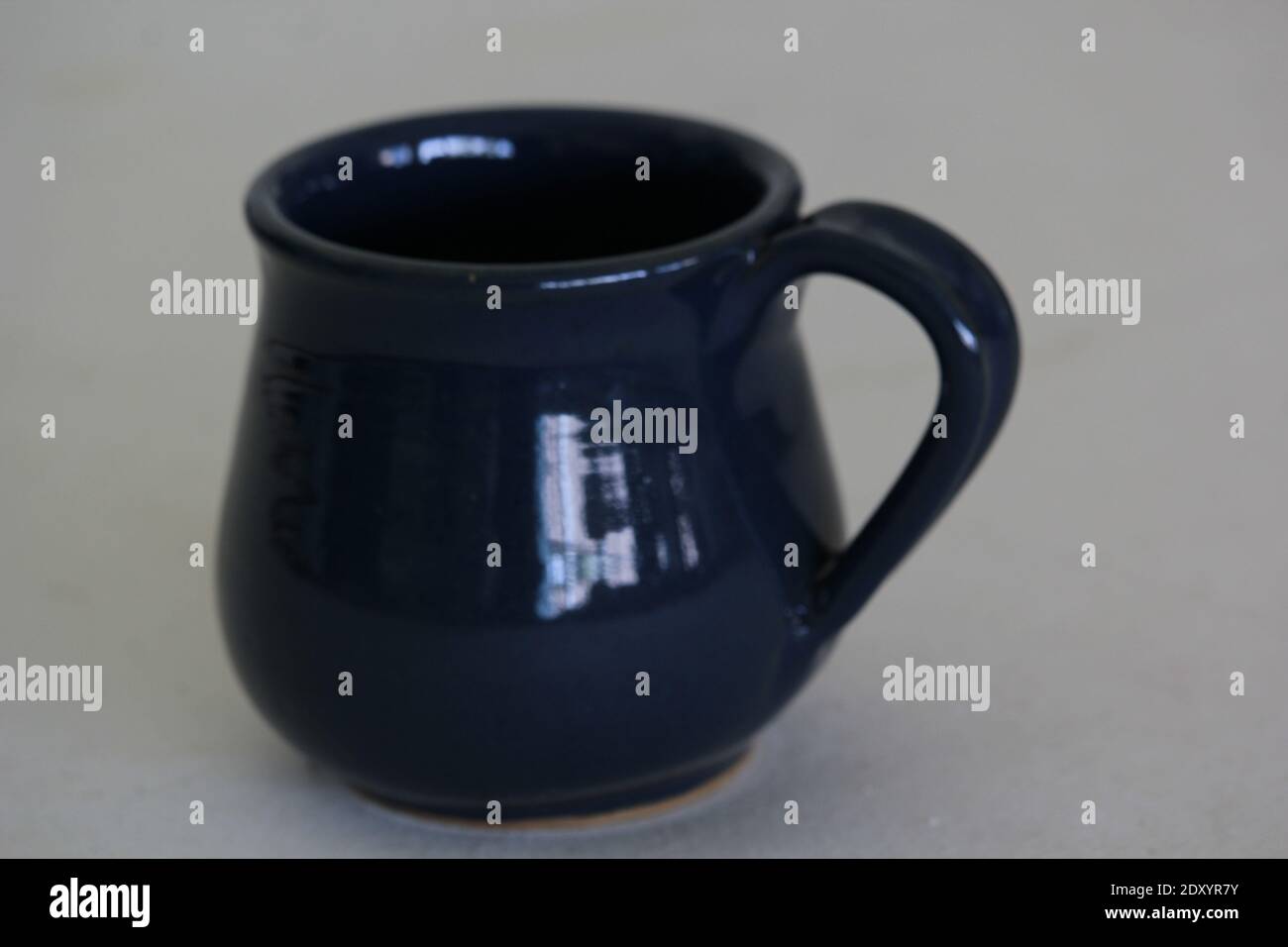 Un primo piano di una tazza di ceramica blu scuro su un sfondo grigio Foto Stock