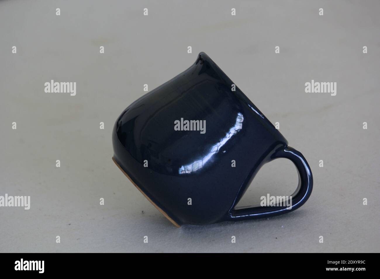 Un primo piano di una tazza di ceramica blu scuro su un sfondo grigio Foto Stock