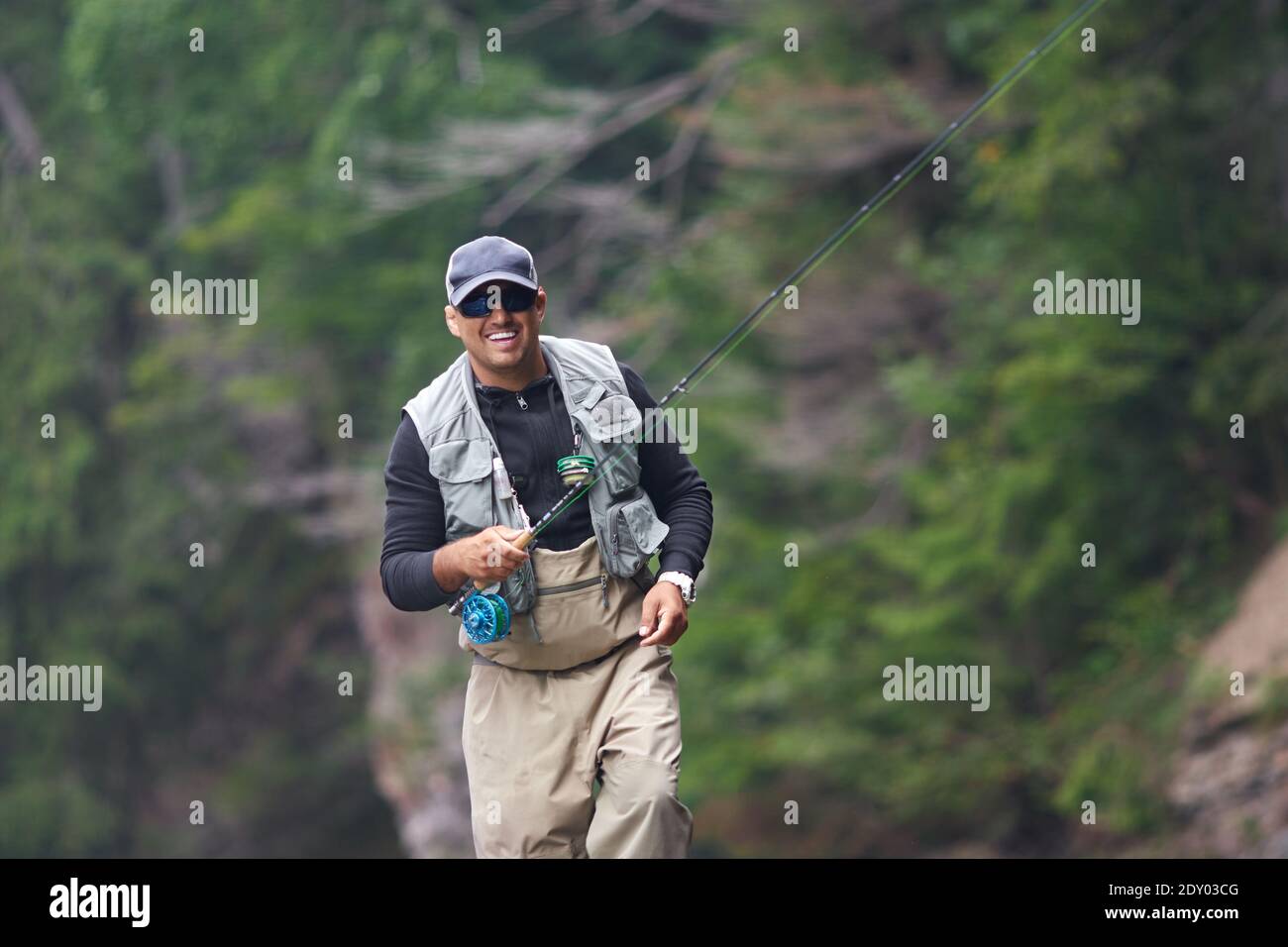 Uomo allegro in berretto e attrezzatura impermeabile pesca in fiume ruvido  tra le belle montagne. Concetto di tempo libero e hobby Foto stock - Alamy