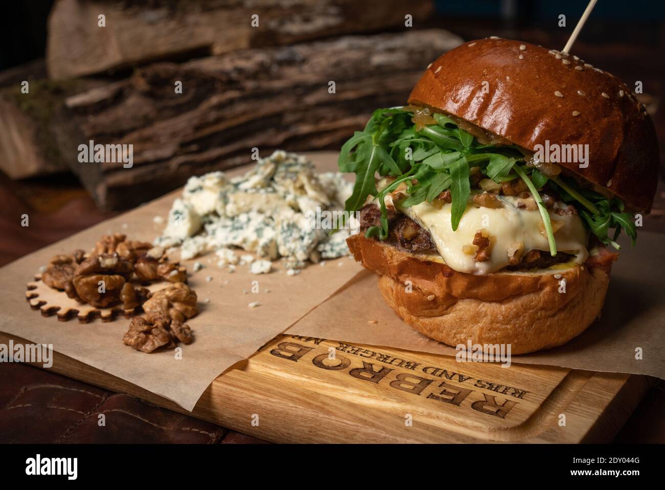 Servito hamburger di manzo artigianale con rucola, noci fresche e formaggio blu posa accanto ad esso. Concetto di ristorante. Concetto di Street food Foto Stock
