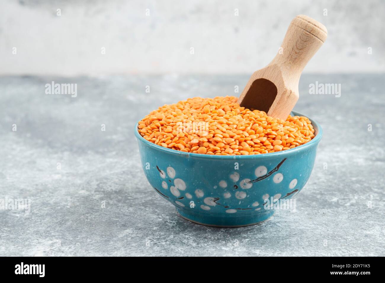 Ciotola di lenticchie rosse grezze su fondo di marmo con cucchiaio Foto Stock