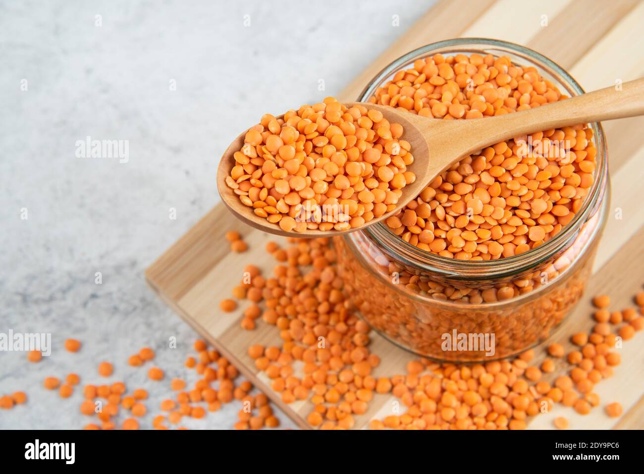 Vaso di vetro di lenticchie rosse con cucchiaio di legno su legno scheda Foto Stock