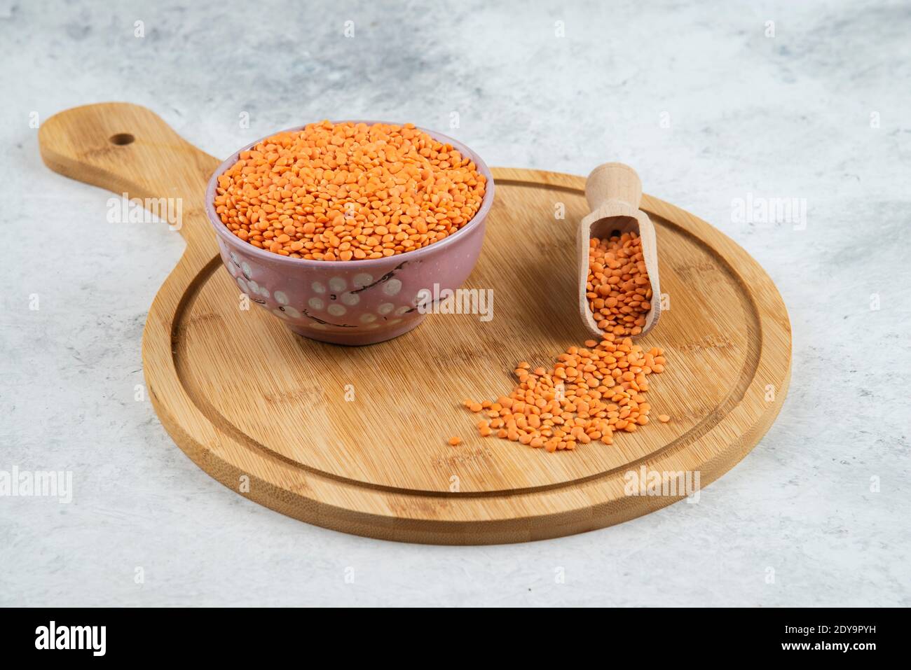Ciotola di lenticchie rosse grezze e cucchiaio sul tagliere Foto Stock