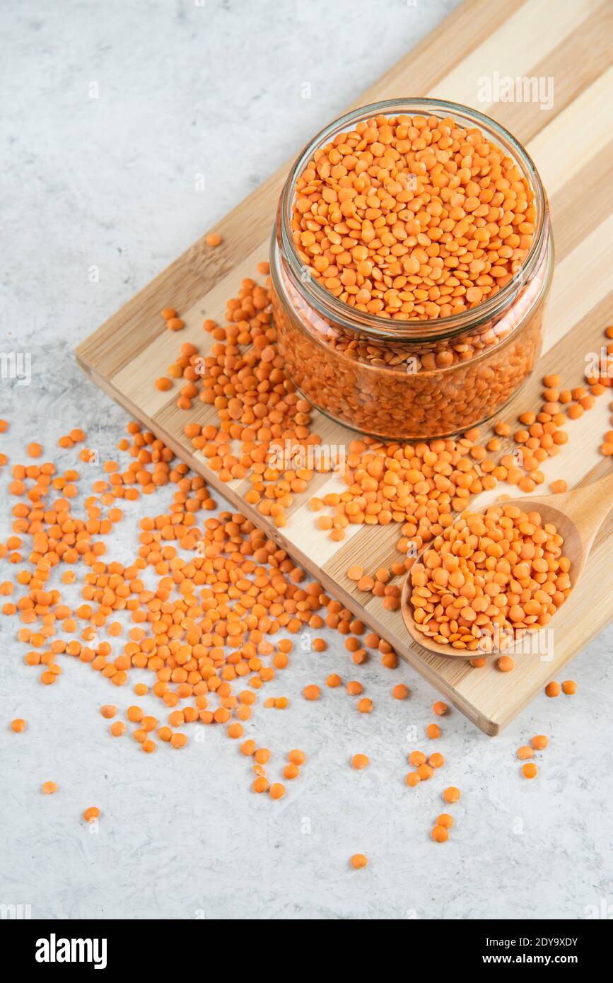 Vaso di vetro di lenticchie rosse su tavola di legno Foto Stock