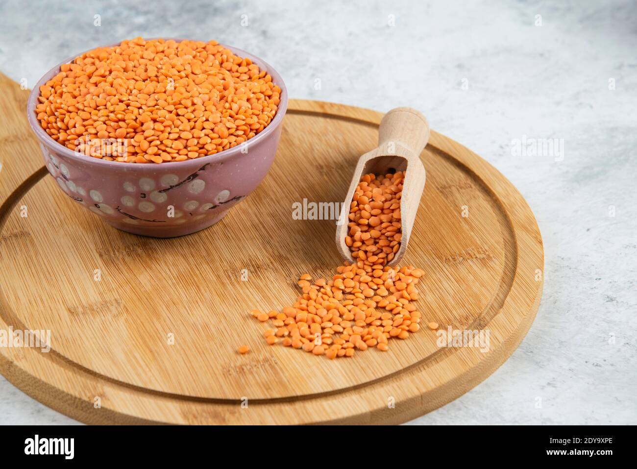 Ciotola di lenticchie grezze e cucchiaio sul tagliere Foto Stock