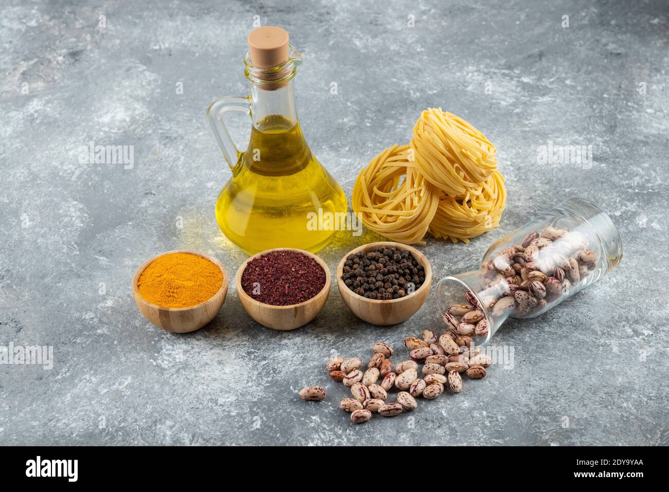 Un vaso di vetro con fagioli bianchi grezzi e grezzi nidi la pasta su uno sfondo grigio Foto Stock