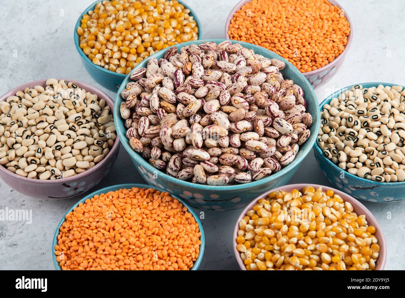 Mazzetto di vari fagioli, cornetti e lenticchie rosse non cotti sulla superficie del marmo Foto Stock