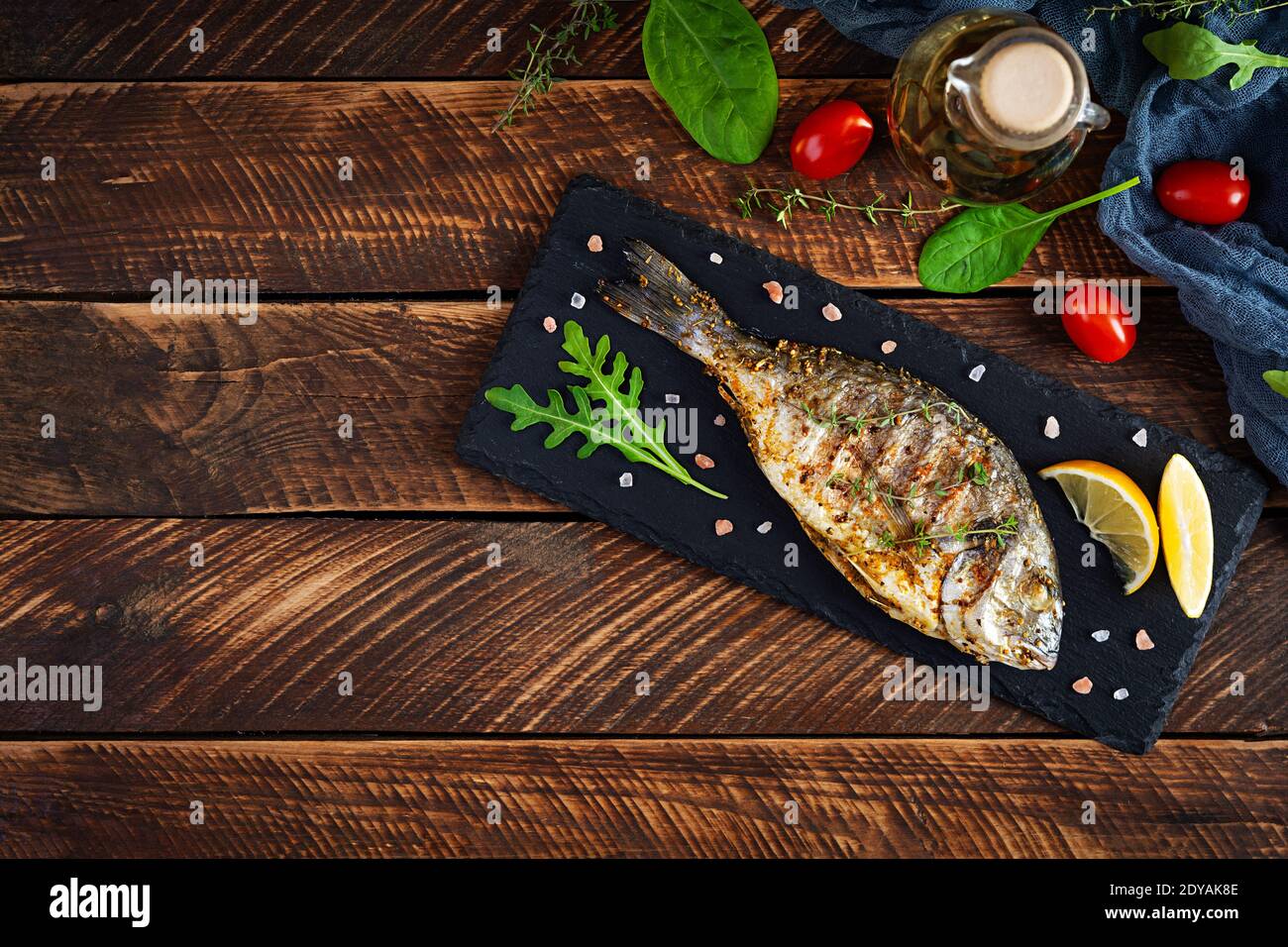 Pesce dorado alla griglia su sfondo di legno. Pesce arrosto con spezie ed erbe Foto Stock